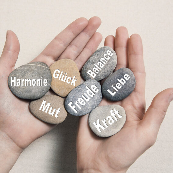 Hände halten Steine mit Glück, Mut, Kraft, Freude, Harmonie